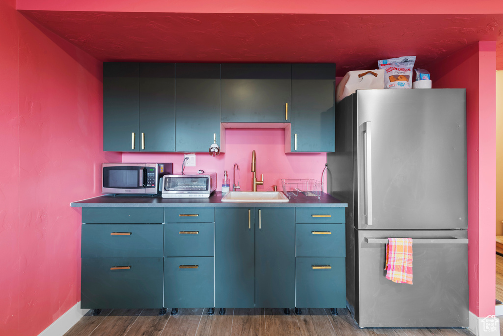 Kitchen with appliances with stainless steel finishes, a sink, dark wood finished floors, blue cabinets, and baseboards
