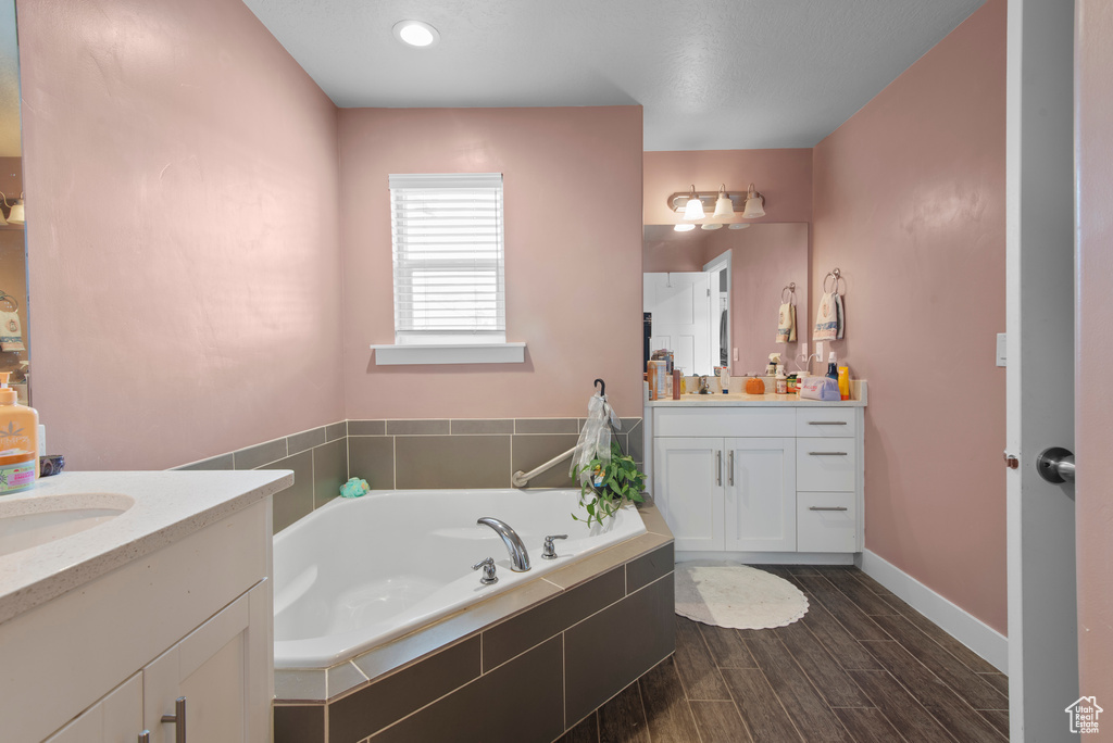 Full bathroom featuring two vanities, a bath, wood finished floors, and baseboards