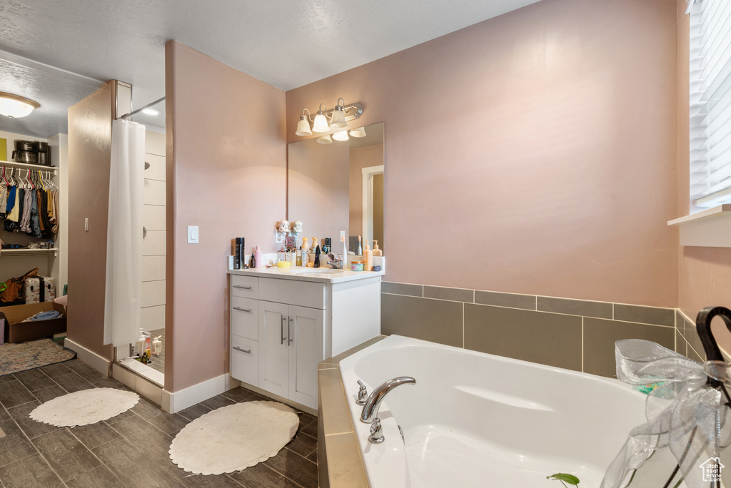 Full bath with vanity, a garden tub, a walk in closet, a stall shower, and wood tiled floors
