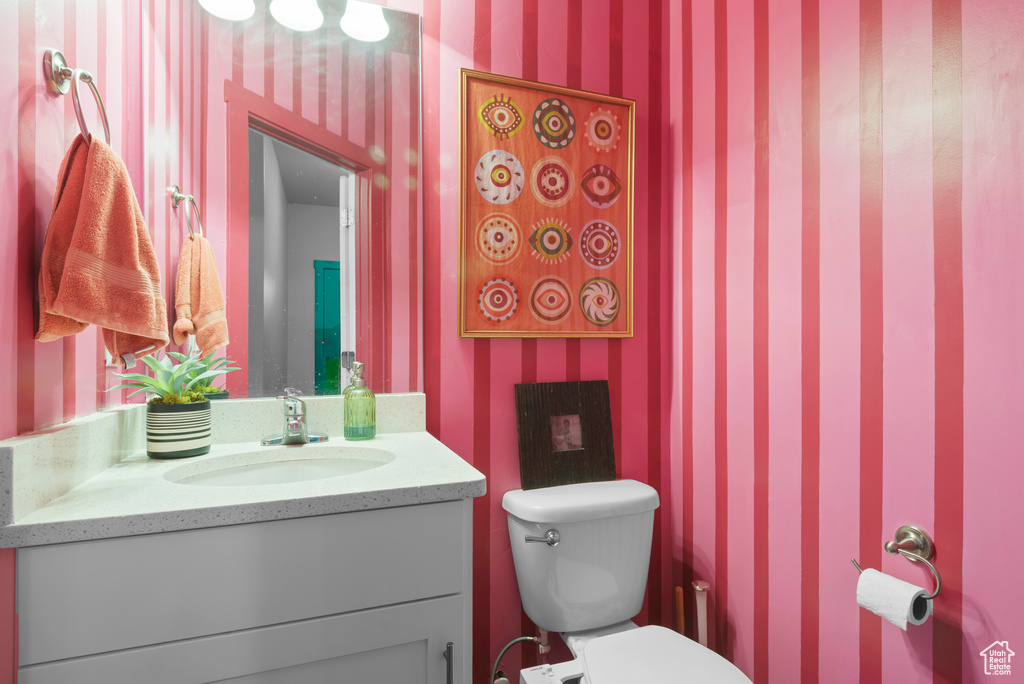 Half bathroom with wallpapered walls, vanity, and toilet