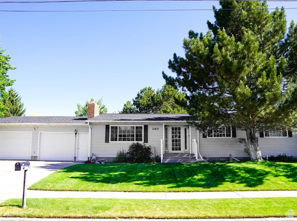 Ranch-style home featuring a garage, concrete driveway, a front lawn, and a chimney