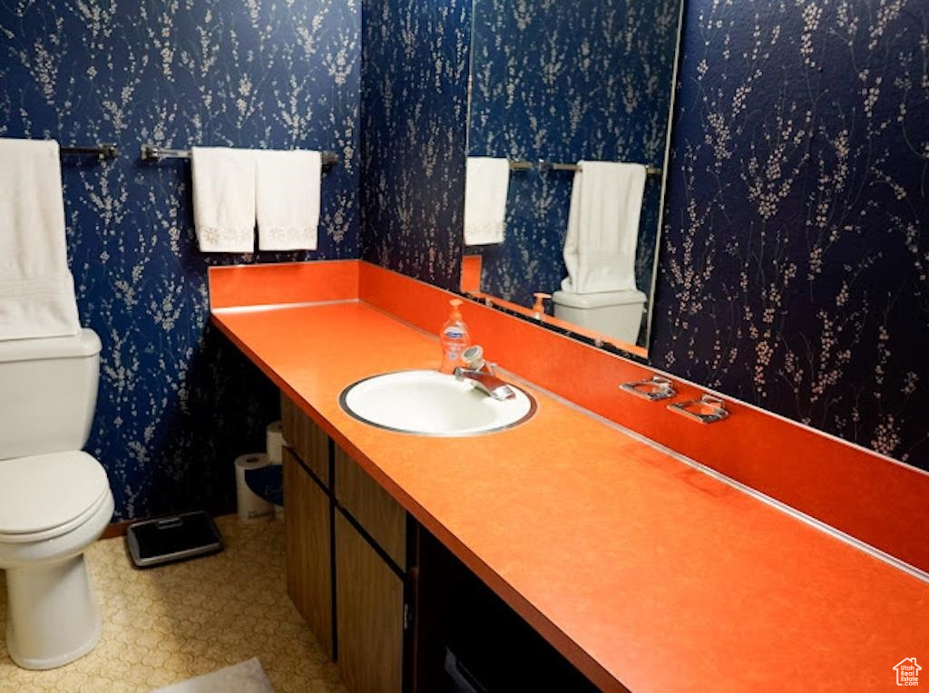 Bathroom featuring toilet, wallpapered walls, vanity, and baseboards