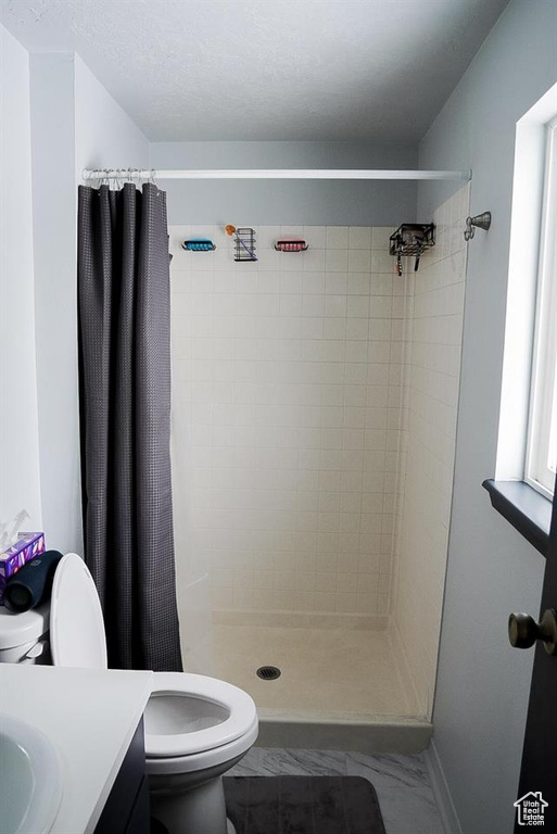 Full bath with toilet, vanity, a stall shower, baseboards, and marble look tiles