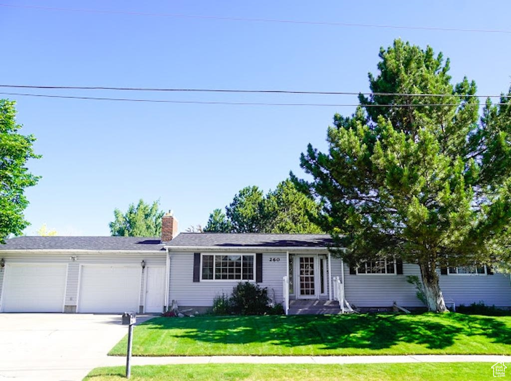 Single story home with an attached garage, driveway, a front yard, and a chimney