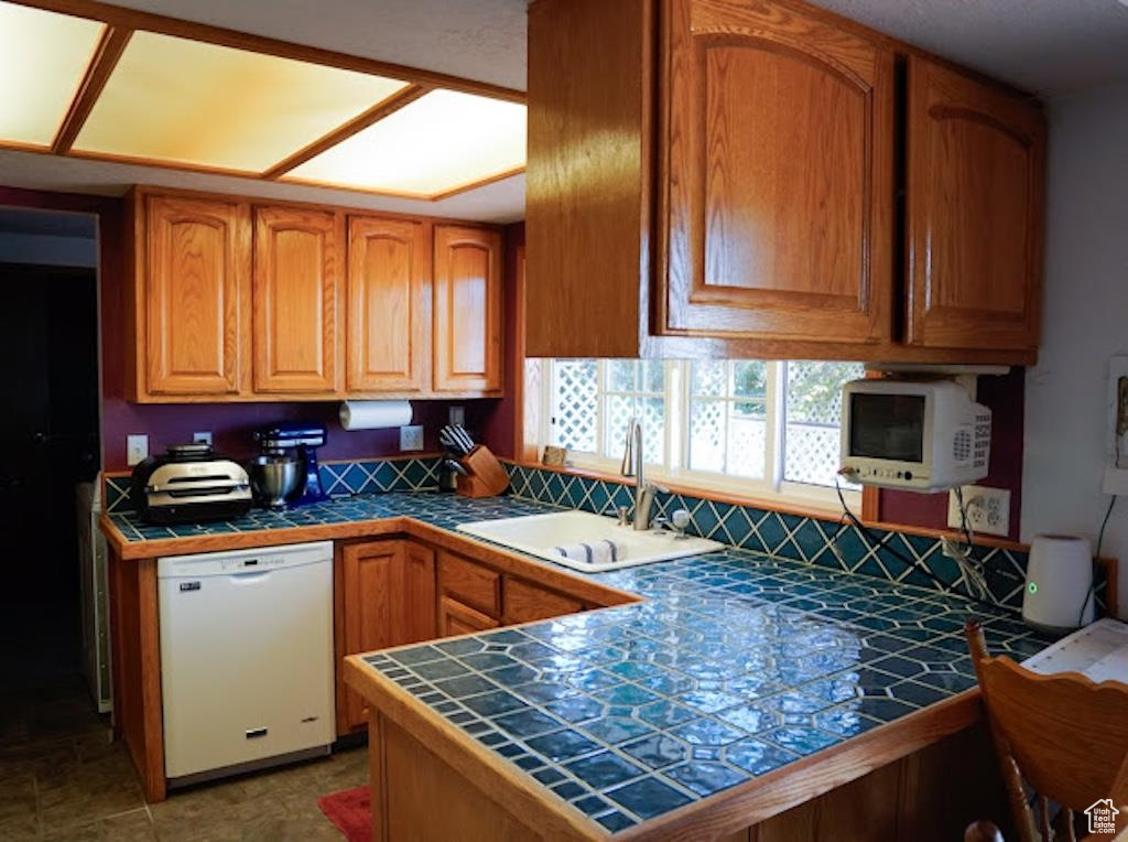 Kitchen featuring dishwasher, tile counters, a sink, and a peninsula