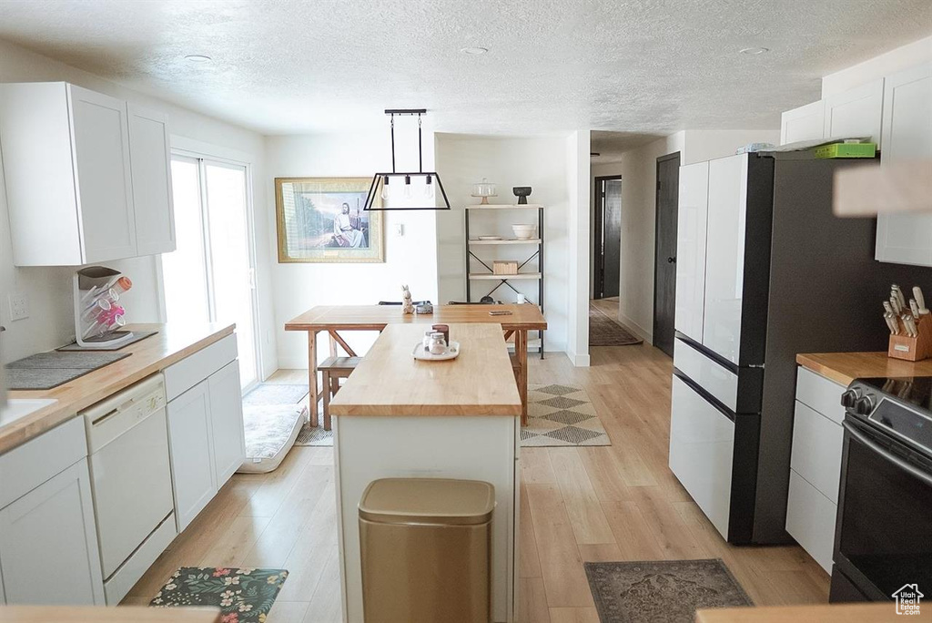 Kitchen with butcher block countertops, dishwasher, black electric range, light wood-type flooring, and a textured ceiling