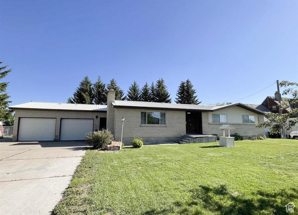 Ranch-style home featuring an attached garage, concrete driveway, a front lawn, a chimney, and brick siding