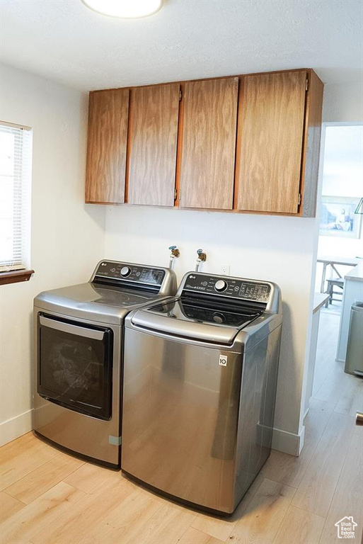 Laundry area with cabinet space, light wood-type flooring, washer and dryer, and baseboards