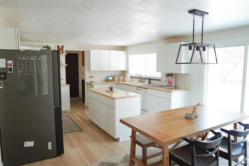 Kitchen with freestanding refrigerator, light wood-style flooring, white cabinetry, dishwasher, and a sink