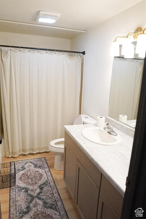 Full bath with toilet, vanity, wood finished floors, and a shower with shower curtain