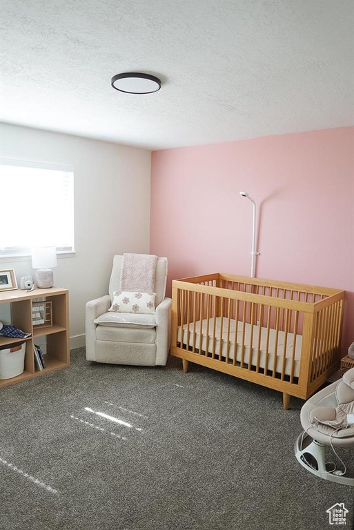Carpeted bedroom featuring a textured ceiling and a crib