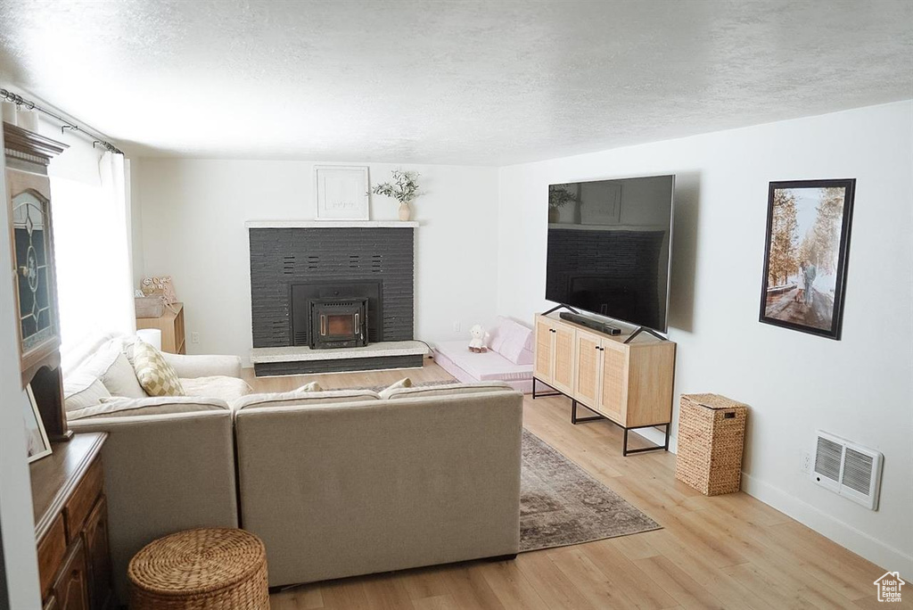 Living room featuring light wood finished floors, baseboards, a fireplace, and a textured ceiling