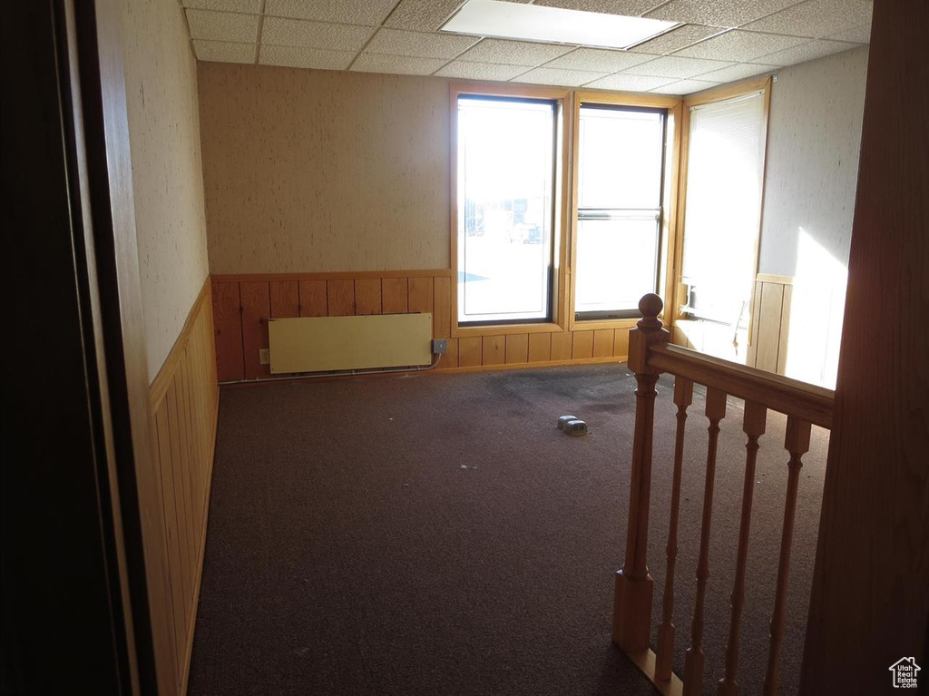 Carpeted spare room with radiator, a paneled ceiling, plenty of natural light, and wainscoting