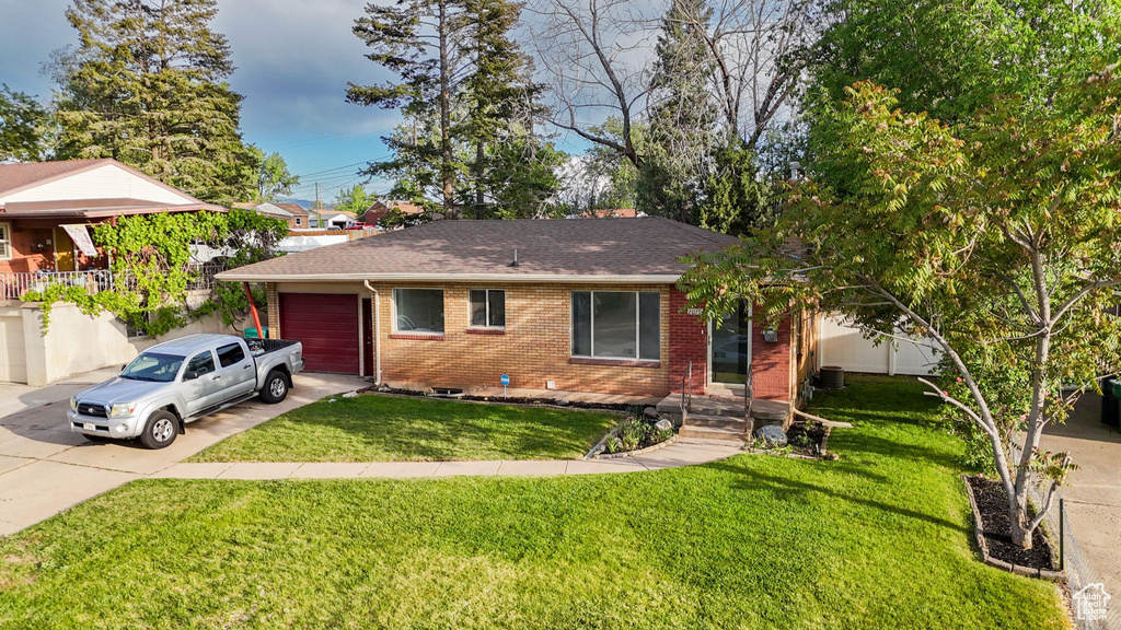 View of front facade with brick siding, concrete driveway, a garage, a shingled roof, and a front yard