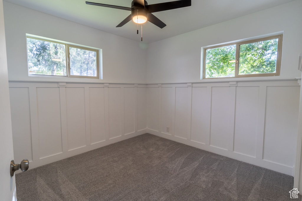 Unfurnished room featuring a decorative wall, a ceiling fan, carpet, and a wainscoted wall