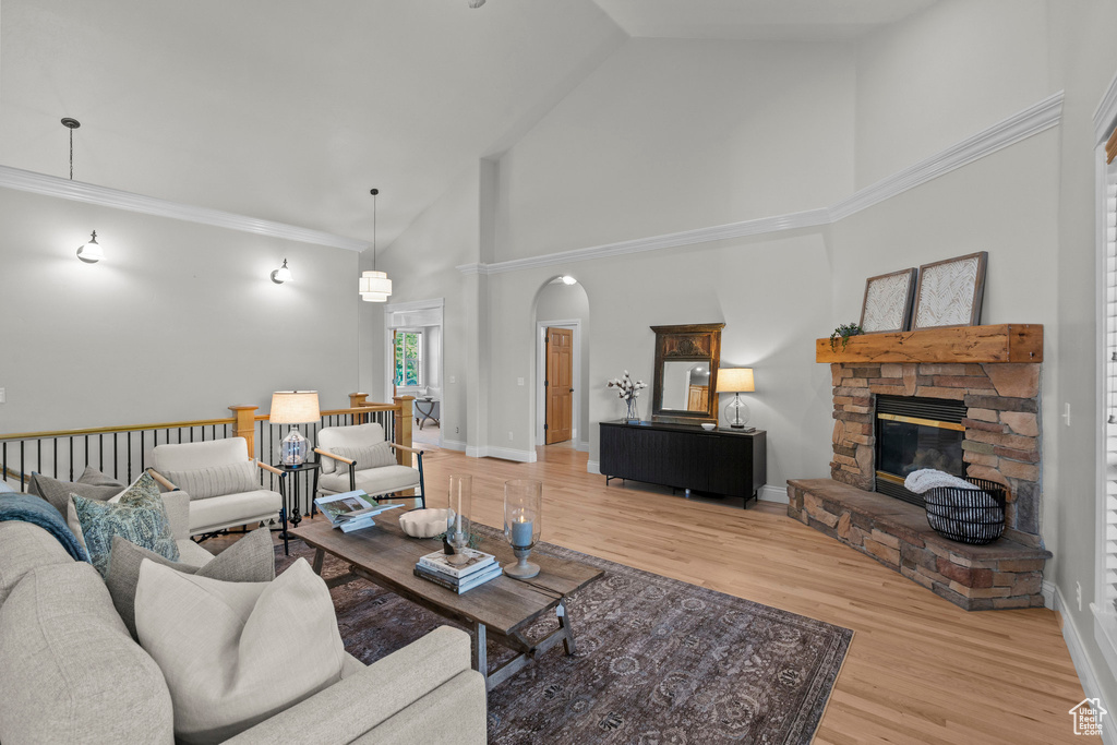 Living area featuring high vaulted ceiling, wood finished floors, a stone fireplace, arched walkways, and baseboards