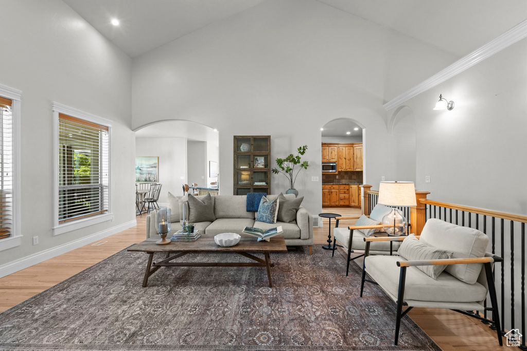 Living area with arched walkways, light wood-style flooring, high vaulted ceiling, baseboards, and recessed lighting