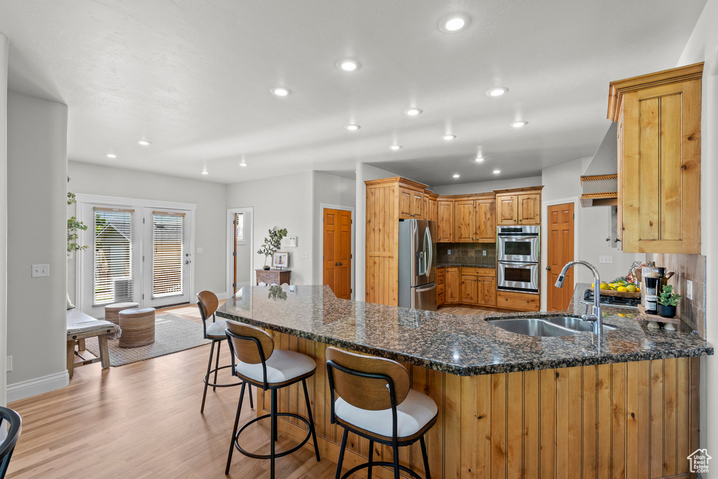 Kitchen featuring a sink, stainless steel appliances, a peninsula, recessed lighting, and light wood-style flooring