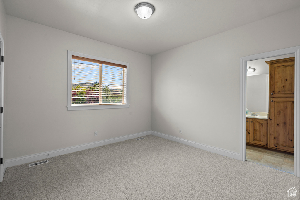 Unfurnished bedroom featuring light carpet, baseboards, ensuite bathroom, and a sink