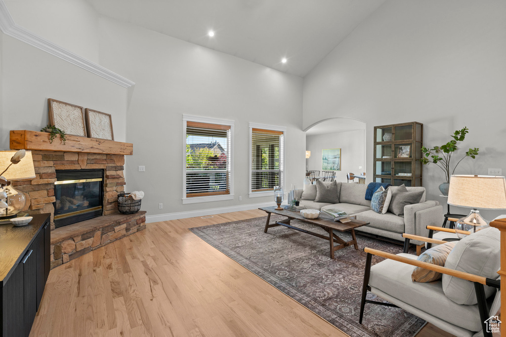 Living area featuring arched walkways, high vaulted ceiling, light wood-style floors, a fireplace, and baseboards