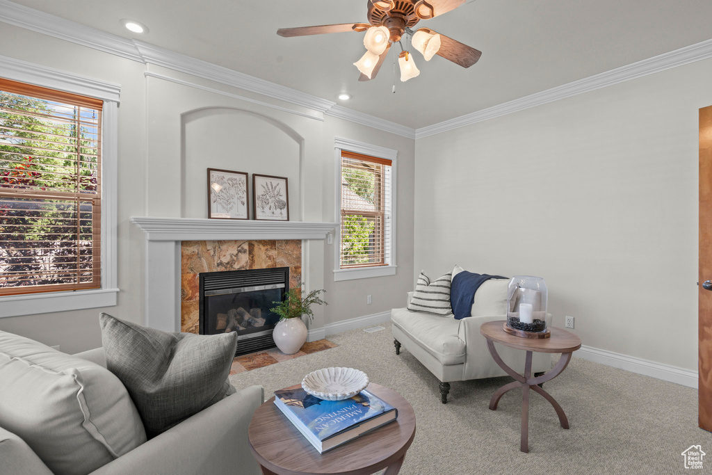 Living room with a ceiling fan, a tiled fireplace, ornamental molding, baseboards, and carpet flooring