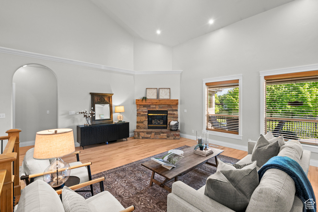 Living room featuring high vaulted ceiling, arched walkways, wood finished floors, a stone fireplace, and baseboards