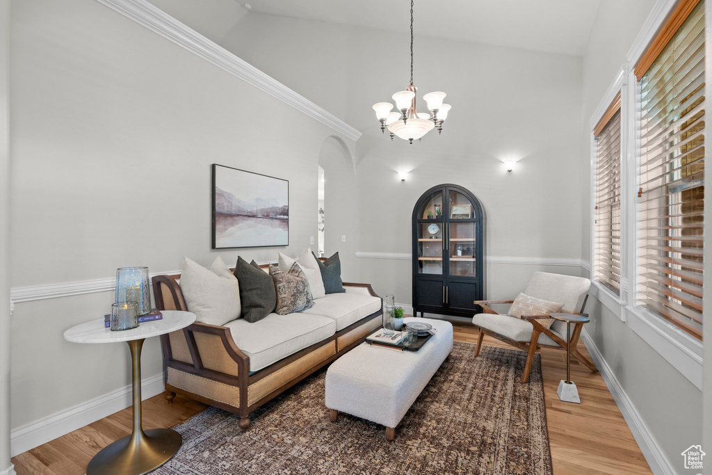 Living room with arched walkways, wood finished floors, a chandelier, baseboards, and high vaulted ceiling