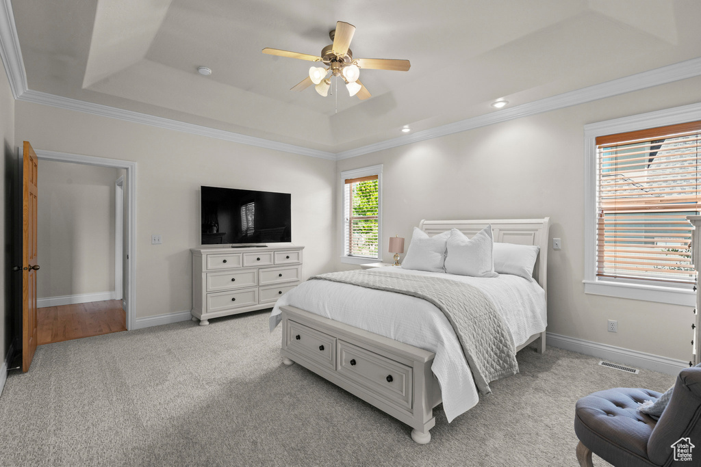 Bedroom featuring a tray ceiling, light carpet, ceiling fan, crown molding, and baseboards