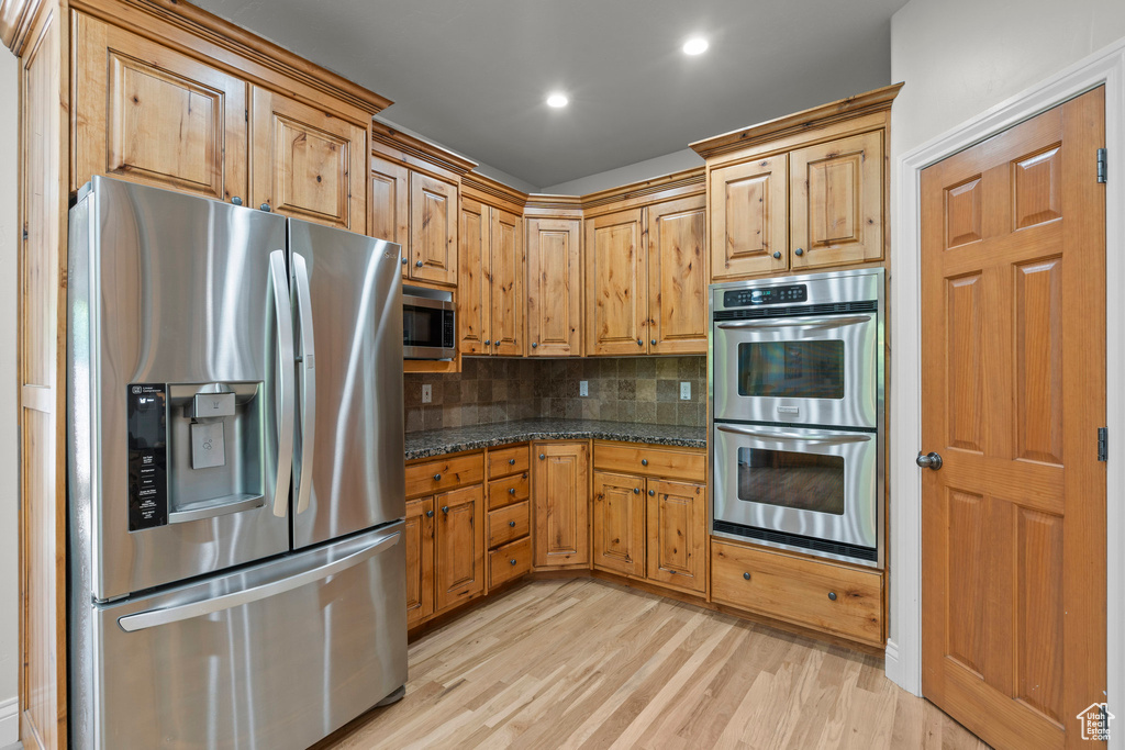 Kitchen with stainless steel appliances, decorative backsplash, light wood-type flooring, recessed lighting, and dark stone countertops