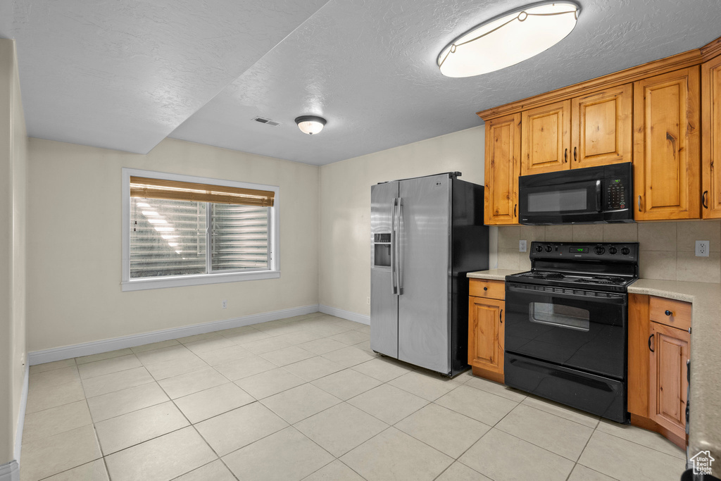 Kitchen featuring black appliances, light countertops, baseboards, backsplash, and a textured ceiling