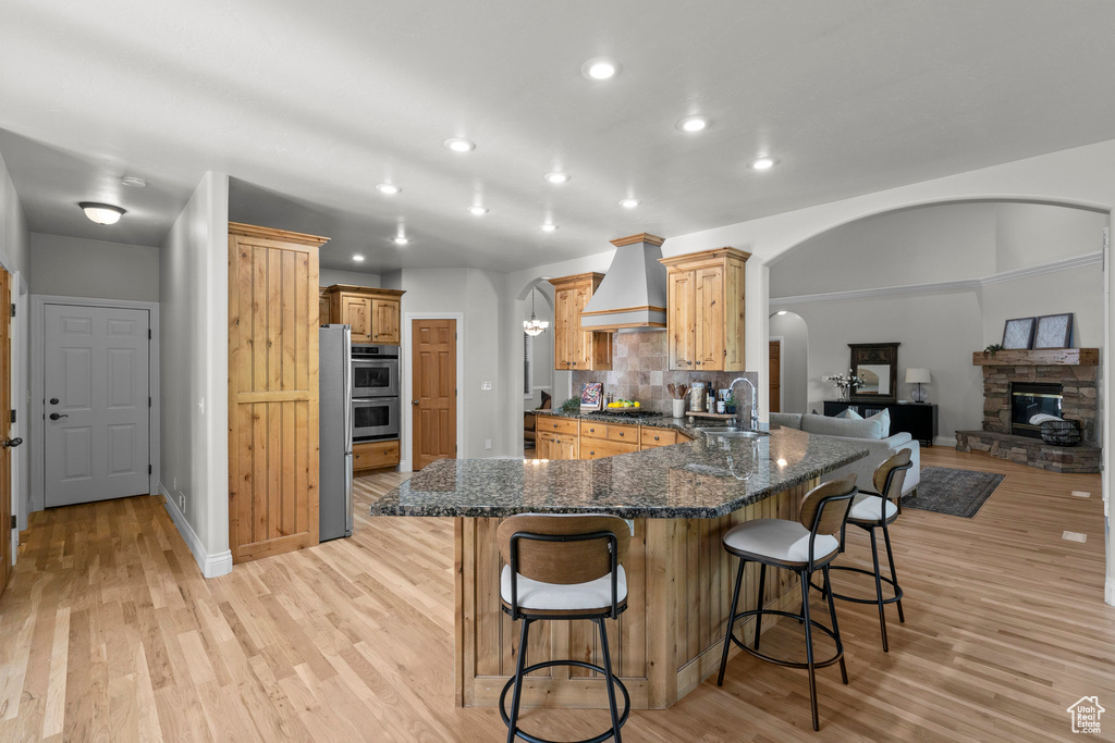 Kitchen featuring custom exhaust hood, arched walkways, light wood-style flooring, and recessed lighting