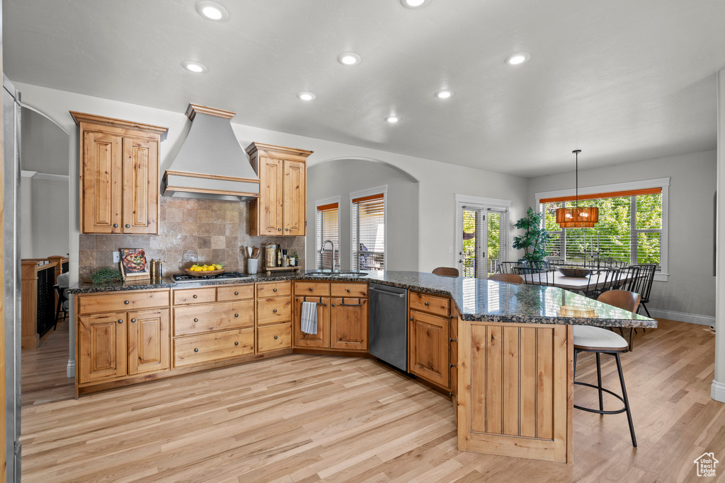 Kitchen with dishwashing machine, a sink, custom range hood, a peninsula, and a kitchen breakfast bar
