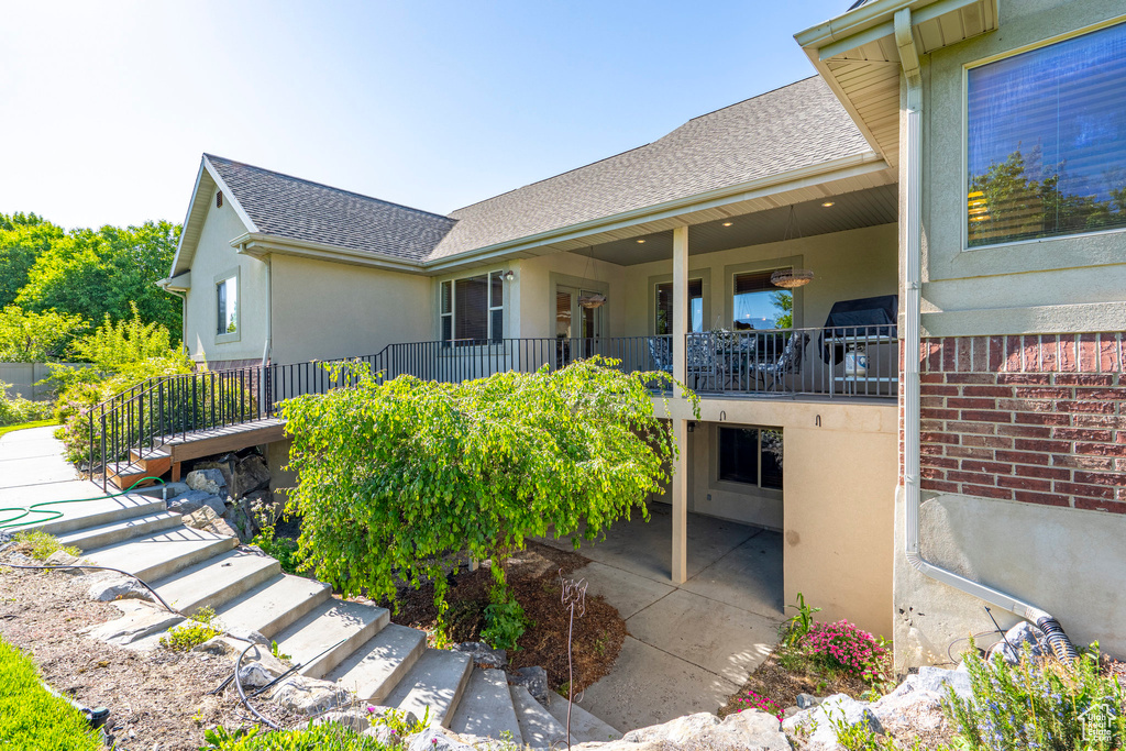 Rear view of house featuring stairs, stucco siding, and roof with shingles