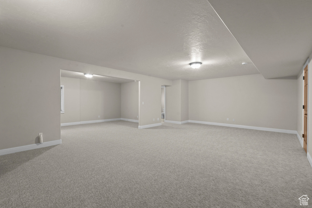 Finished below grade area with light carpet, baseboards, and a textured ceiling