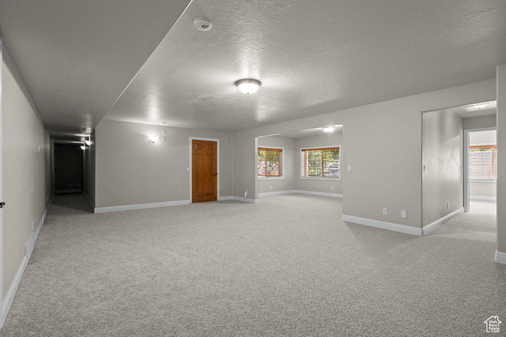 Spare room with a textured ceiling, baseboards, light colored carpet, and healthy amount of natural light