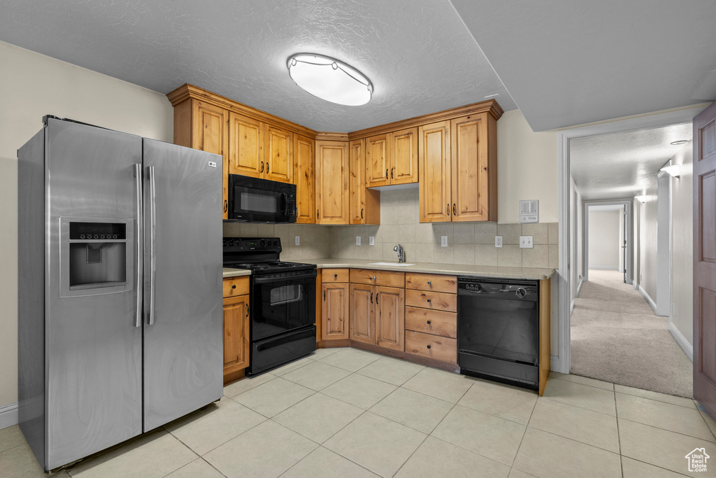 Kitchen with black appliances, light countertops, a sink, tasteful backsplash, and light tile patterned floors