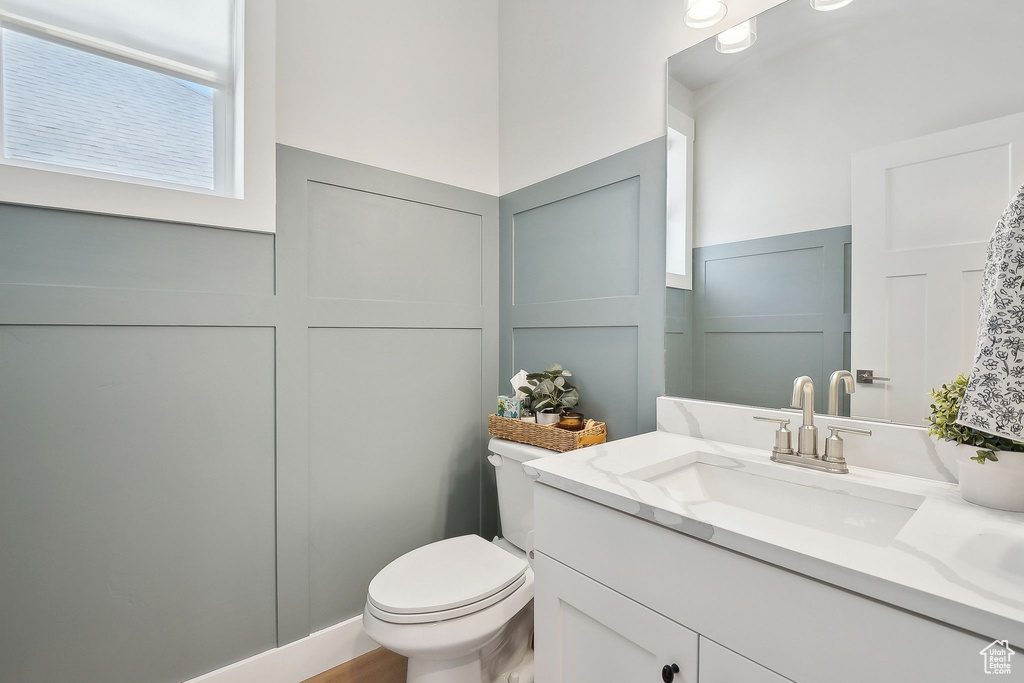 Bathroom featuring a decorative wall, vanity, toilet, and a wainscoted wall