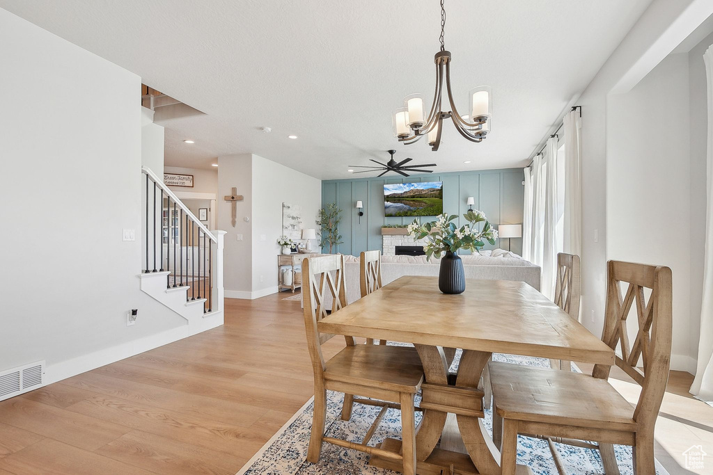 Dining room with a chandelier, light wood finished floors, a ceiling fan, stairs, and baseboards