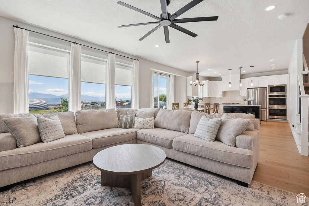 Living area featuring light wood-style floors, a chandelier, recessed lighting, a ceiling fan, and a textured ceiling