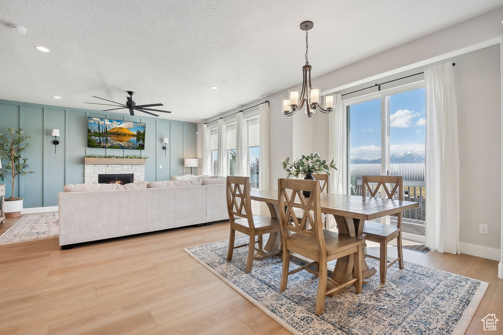 Dining area featuring light wood-style floors, a ceiling fan, a textured ceiling, recessed lighting, and a stone fireplace
