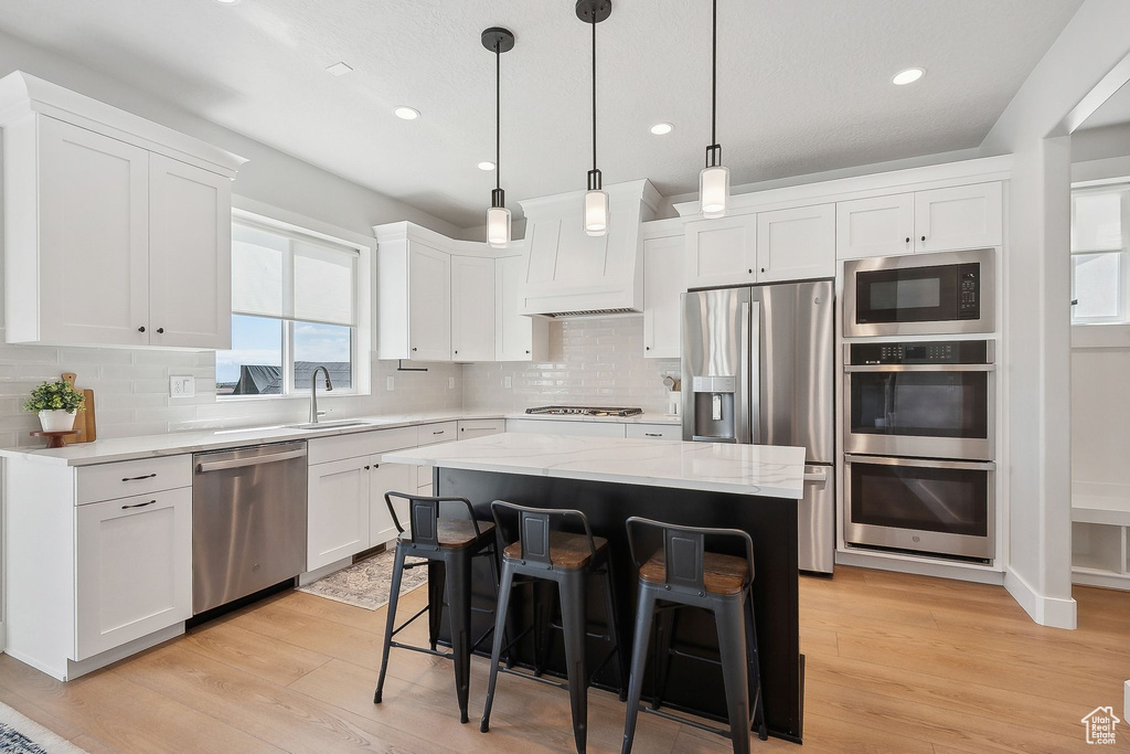Kitchen featuring stainless steel appliances, premium range hood, white cabinetry, light wood-style floors, and recessed lighting