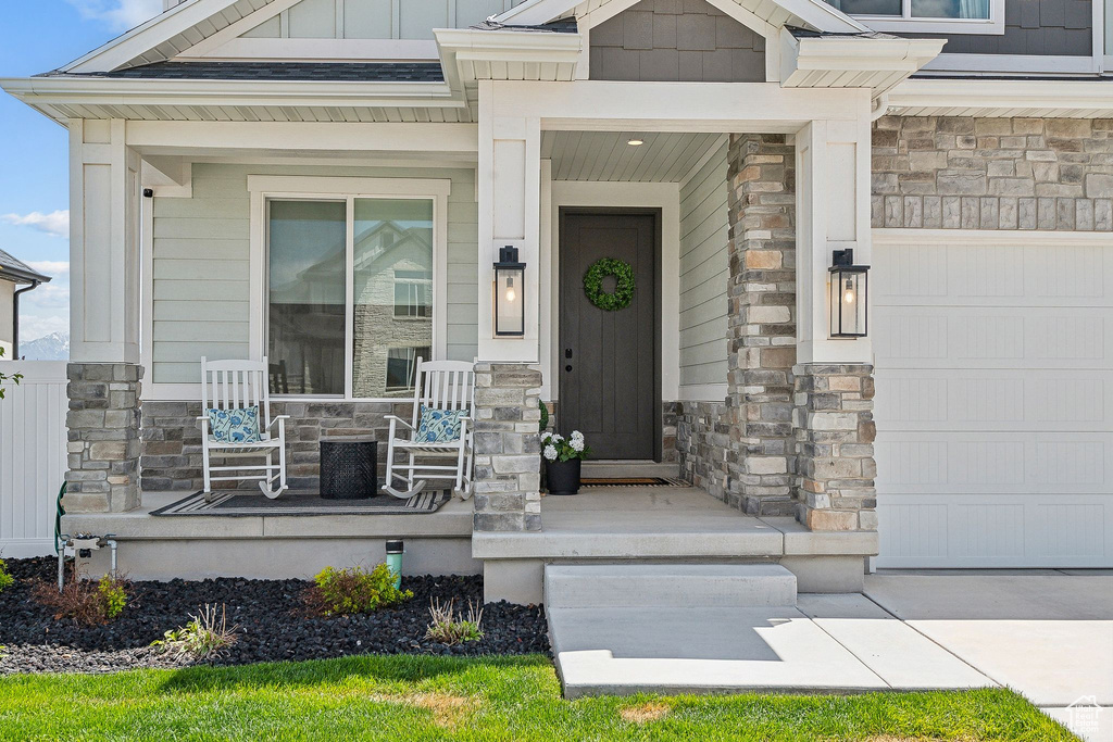 Doorway to property featuring a porch, stone siding, a garage, and board and batten siding