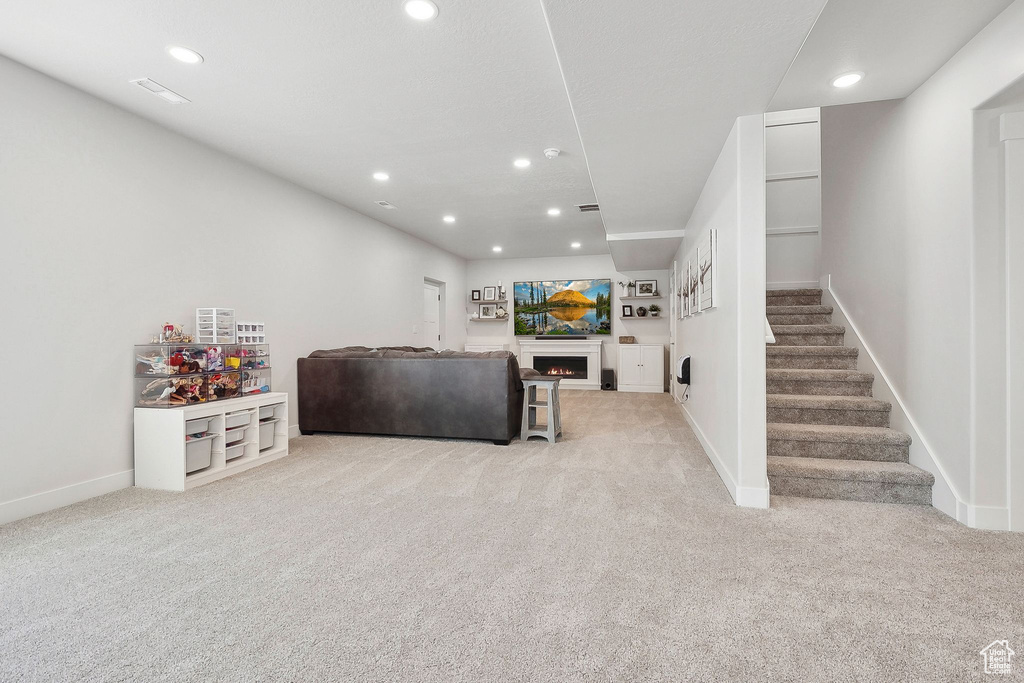 Living room with light carpet, stairs, recessed lighting, baseboards, and a warm lit fireplace