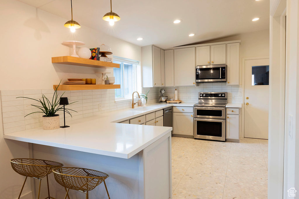 Kitchen featuring stainless steel appliances, a kitchen breakfast bar, a peninsula, tasteful backsplash, and recessed lighting