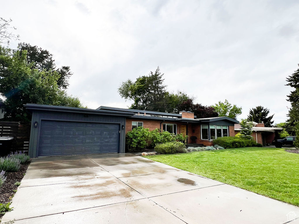 Ranch-style house featuring an attached garage, a chimney, driveway, brick siding, and a front yard