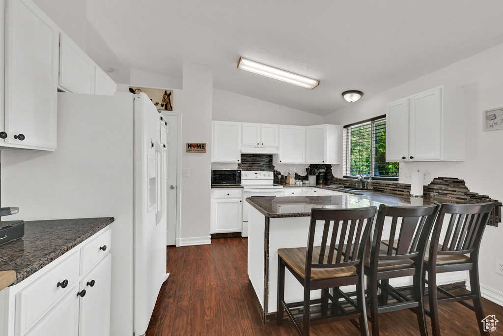Kitchen featuring white appliances, vaulted ceiling, a sink, a kitchen bar, and white cabinetry