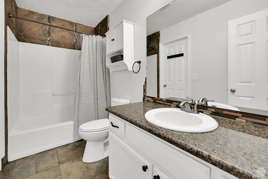Bathroom with toilet, vanity, stone finish flooring, shower / tub combo, and a textured ceiling