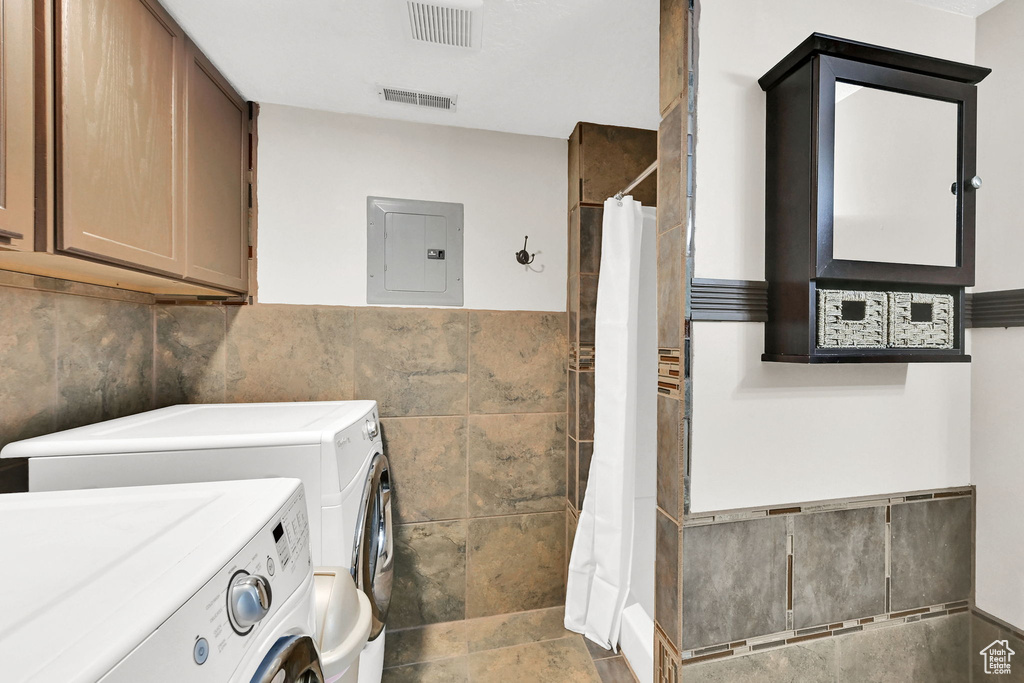 Laundry room with independent washer and dryer, tile walls, electric panel, cabinet space, and wainscoting