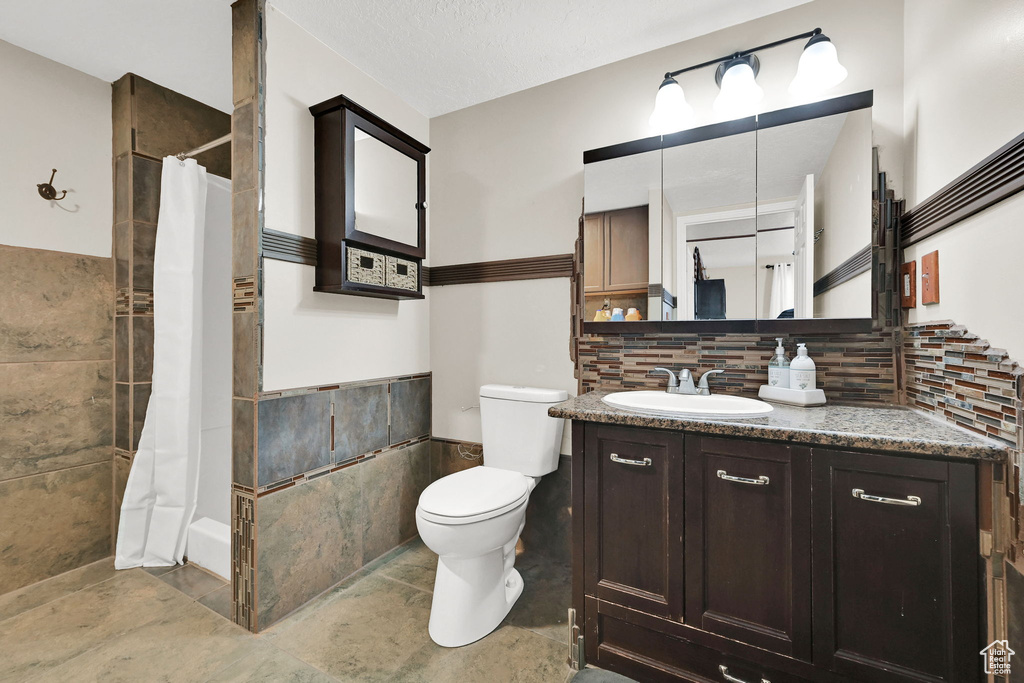 Bathroom featuring toilet, wainscoting, vanity, a shower with shower curtain, and tile walls