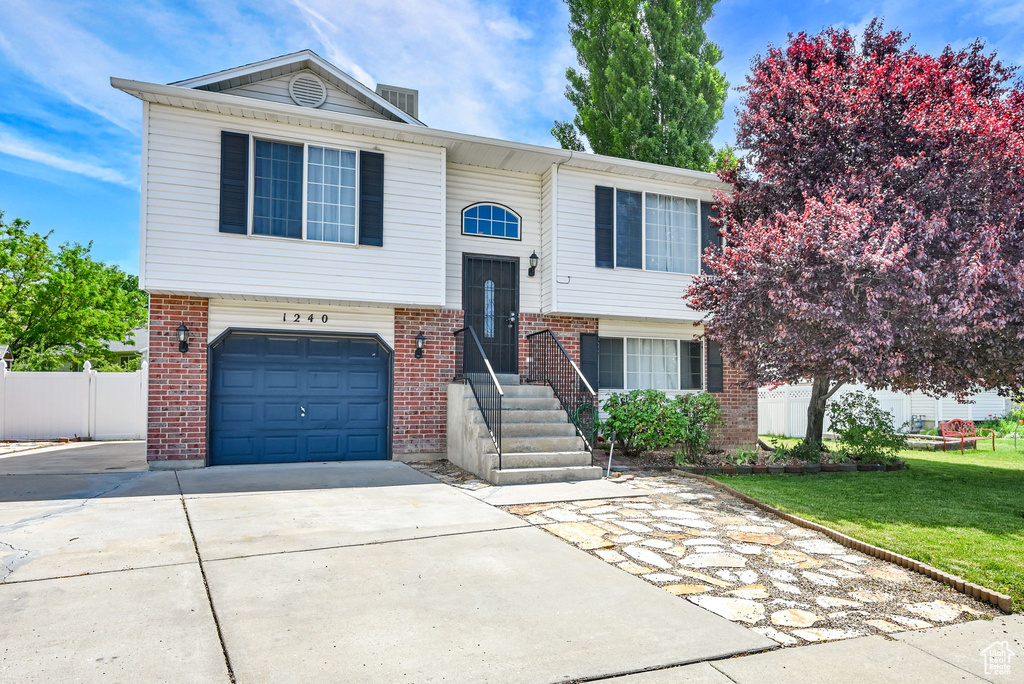 Raised ranch featuring brick siding, concrete driveway, and a garage